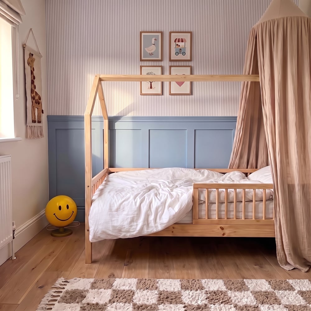 Foto van Noors slaapkamer, nog leeg: een grenen huisjesbed met wit dekbed en een hemeltje, gestreept behang, blauwe lambrisering, vier prentjes, een giraf aan de muur en een gele smileylamp