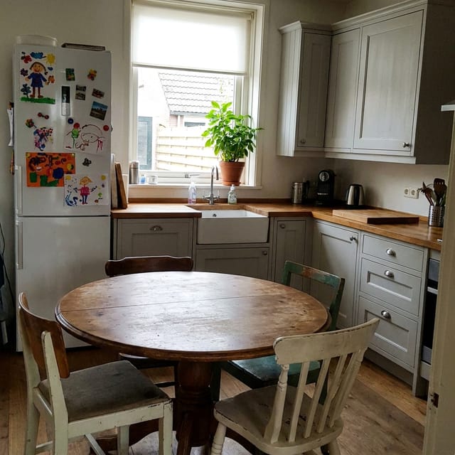 Foto van de keuken: lichtgrijze kastjes, houten aanrecht, ronde eettafel, koelkast met kindertekeningen